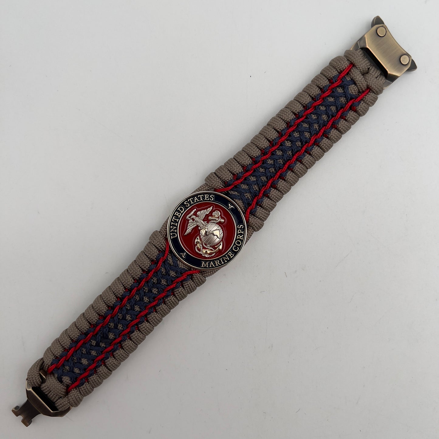 Thick, rigid and comfortable braided United States Marine Corps bracelet featuring a 24K gold and silver plated USMC officer Eagle Globe and Anchor medallion, a gold Cobra style tactical buckle and woven with tan 550 paracord and Imperial Red and Navy Blue micro cord.