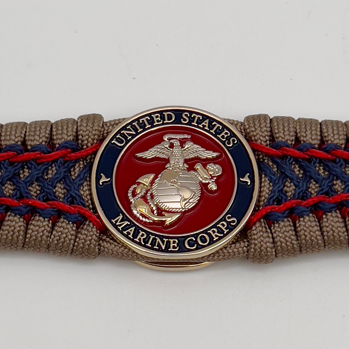 Thick, rigid and comfortable braided United States Marine Corps bracelet featuring a 24K gold and silver plated USMC officer Eagle Globe and Anchor medallion, a gold Cobra style tactical buckle and woven with tan 550 paracord and Imperial Red and Navy Blue micro cord.