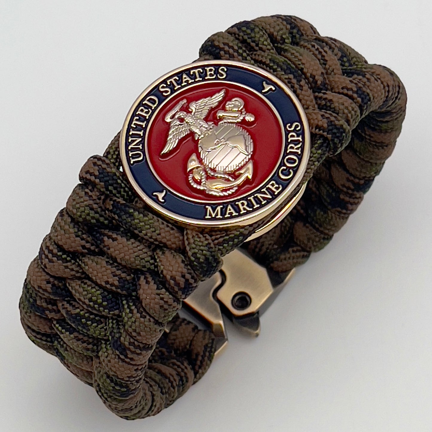 Thick, rigid and comfortable braided United States Marine Corps bracelet featuring a 24K gold and silver plated USMC officer Eagle Globe and Anchor medallion, a gold Cobra style tactical buckle and woven with Woodland Camo 550 paracord.