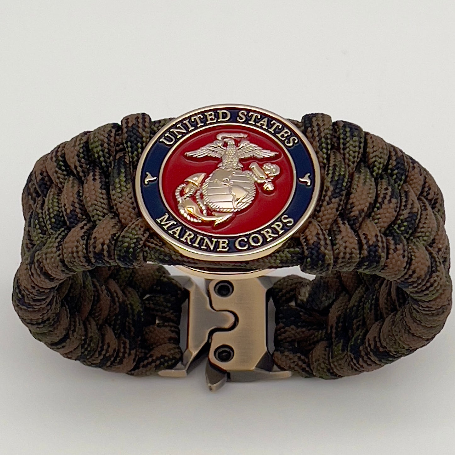 Thick, rigid and comfortable braided United States Marine Corps bracelet featuring a 24K gold and silver plated USMC officer Eagle Globe and Anchor medallion, a gold Cobra style tactical buckle and woven with Woodland Camo 550 paracord.