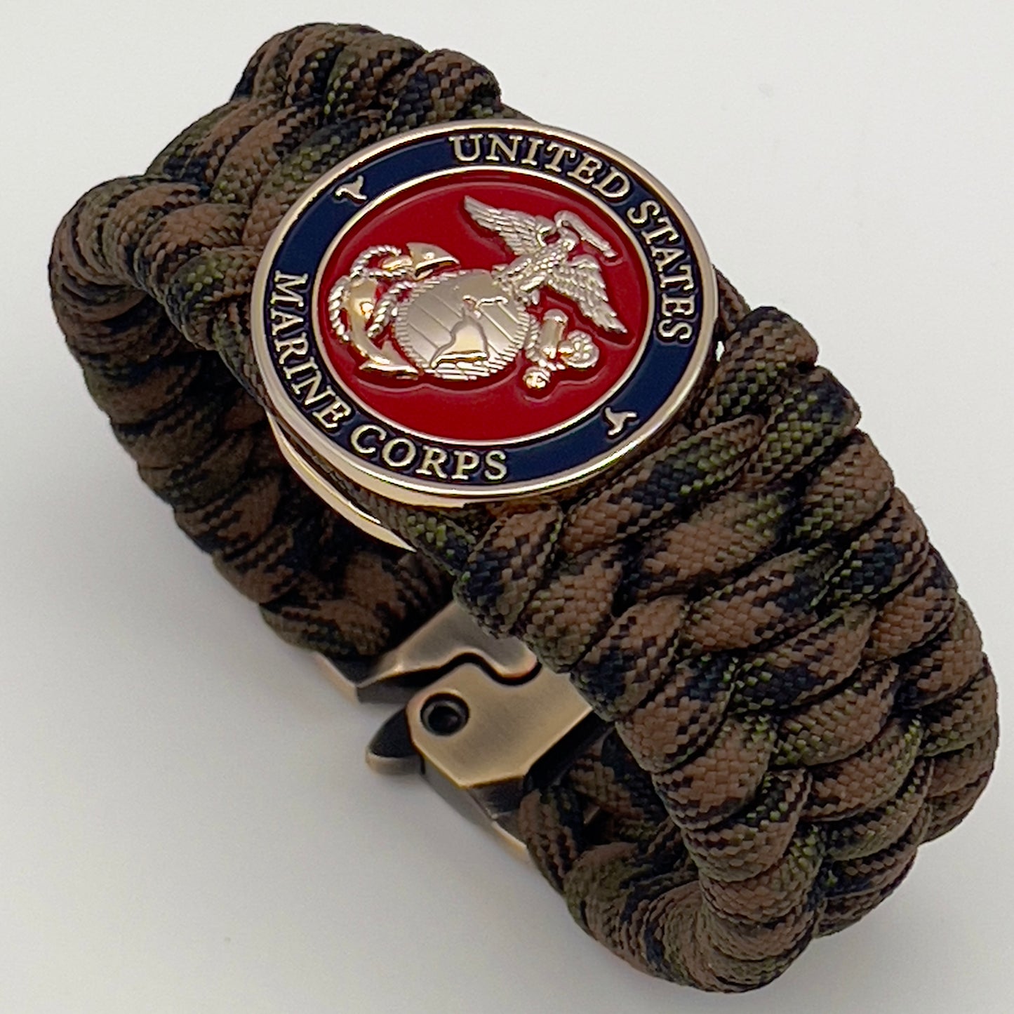 Thick, rigid and comfortable braided United States Marine Corps bracelet featuring a 24K gold and silver plated USMC officer Eagle Globe and Anchor medallion, a gold Cobra style tactical buckle and woven with Woodland Camo 550 paracord.