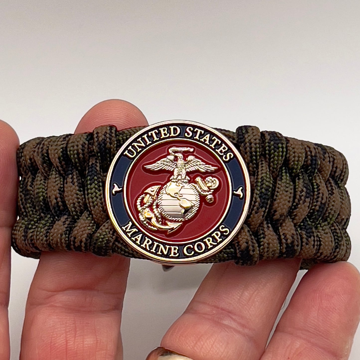 Thick, rigid and comfortable braided United States Marine Corps bracelet featuring a 24K gold and silver plated USMC officer Eagle Globe and Anchor medallion, a gold Cobra style tactical buckle and woven with Woodland Camo 550 paracord.