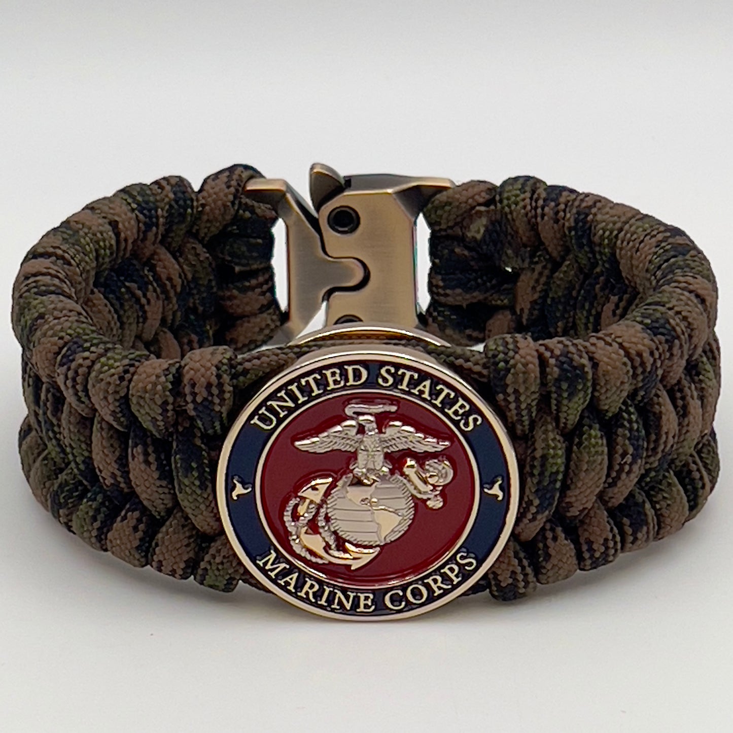 Thick, rigid and comfortable braided United States Marine Corps bracelet featuring a 24K gold and silver plated USMC officer Eagle Globe and Anchor medallion, a gold Cobra style tactical buckle and woven with Woodland Camo 550 paracord.