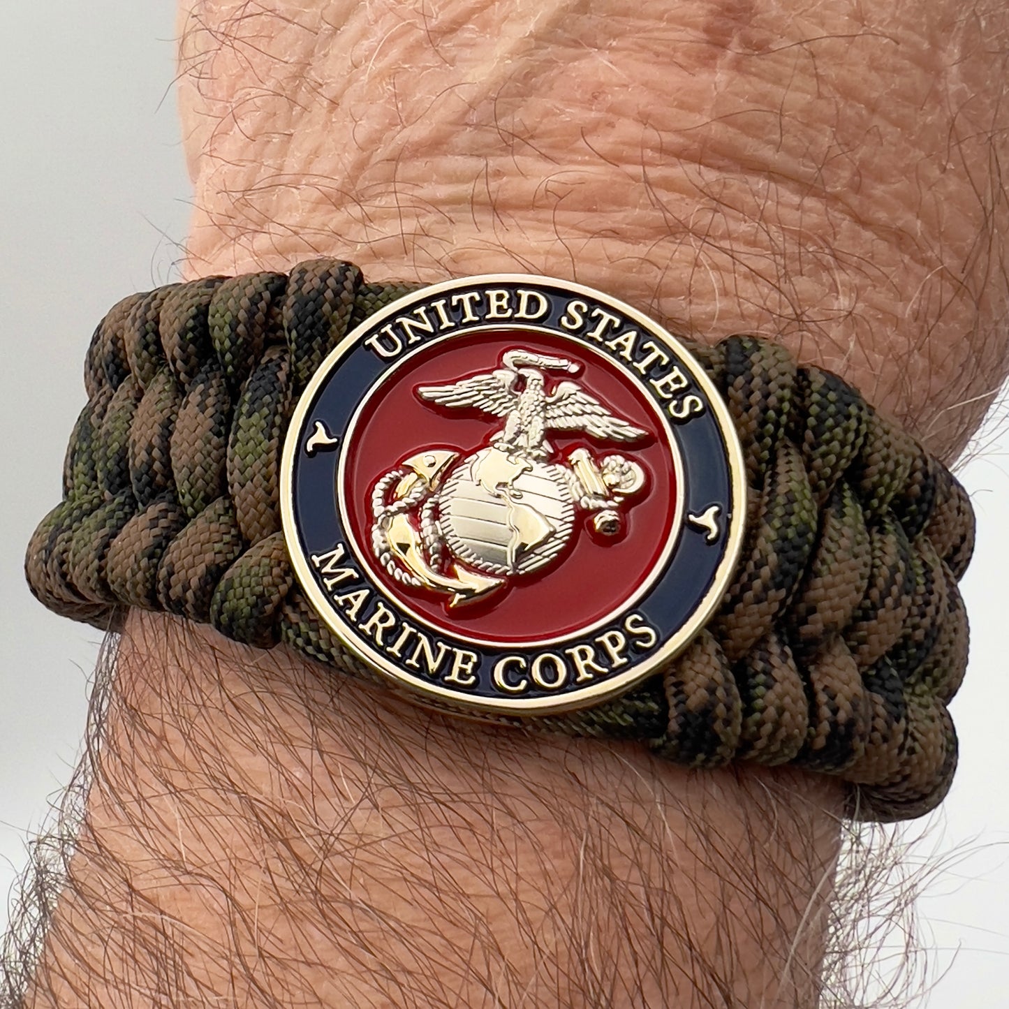 Thick, rigid and comfortable braided United States Marine Corps bracelet featuring a 24K gold and silver plated USMC officer Eagle Globe and Anchor medallion, a gold Cobra style tactical buckle and woven with Woodland Camo 550 paracord.