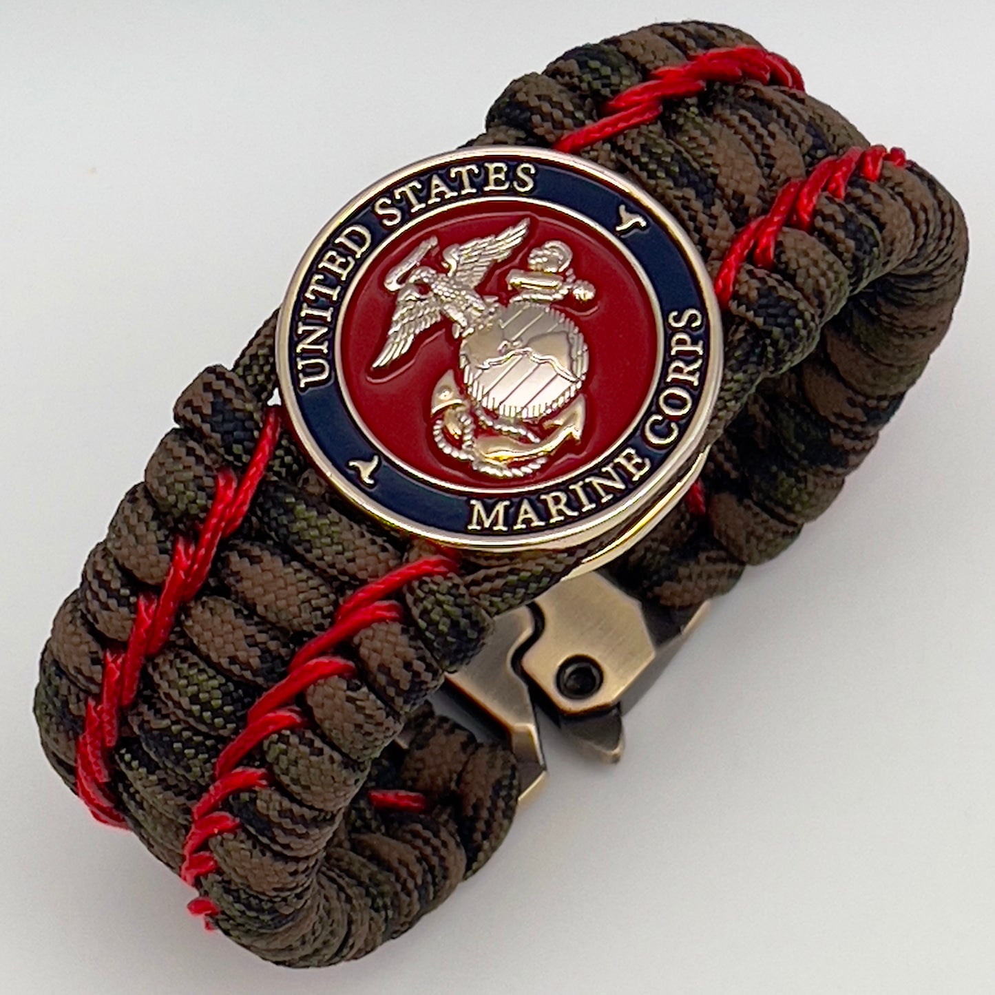 Thick, rigid and comfortable braided United States Marine Corps bracelet featuring a 24K gold and silver plated USMC officer Eagle Globe and Anchor medallion, a gold Cobra style tactical buckle and woven with Woodland Camo 550 paracord and Imperial Red micro cord.