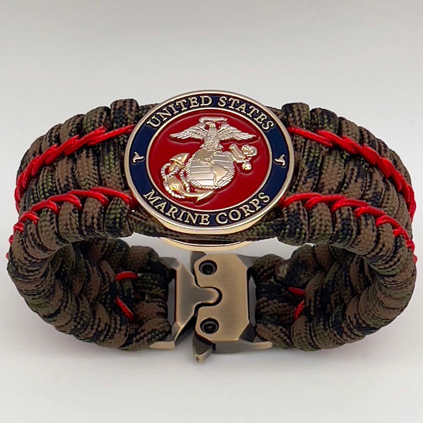 Thick, rigid and comfortable braided United States Marine Corps bracelet featuring a 24K gold and silver plated USMC officer Eagle Globe and Anchor medallion, a gold Cobra style tactical buckle and woven with Woodland Camo 550 paracord and Imperial Red micro cord.