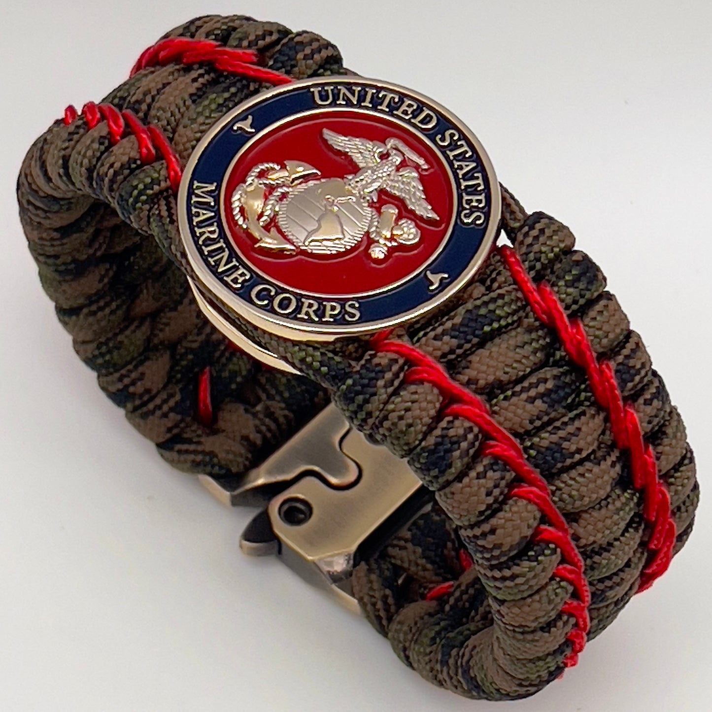 Thick, rigid and comfortable braided United States Marine Corps bracelet featuring a 24K gold and silver plated USMC officer Eagle Globe and Anchor medallion, a gold Cobra style tactical buckle and woven with Woodland Camo 550 paracord and Imperial Red micro cord.