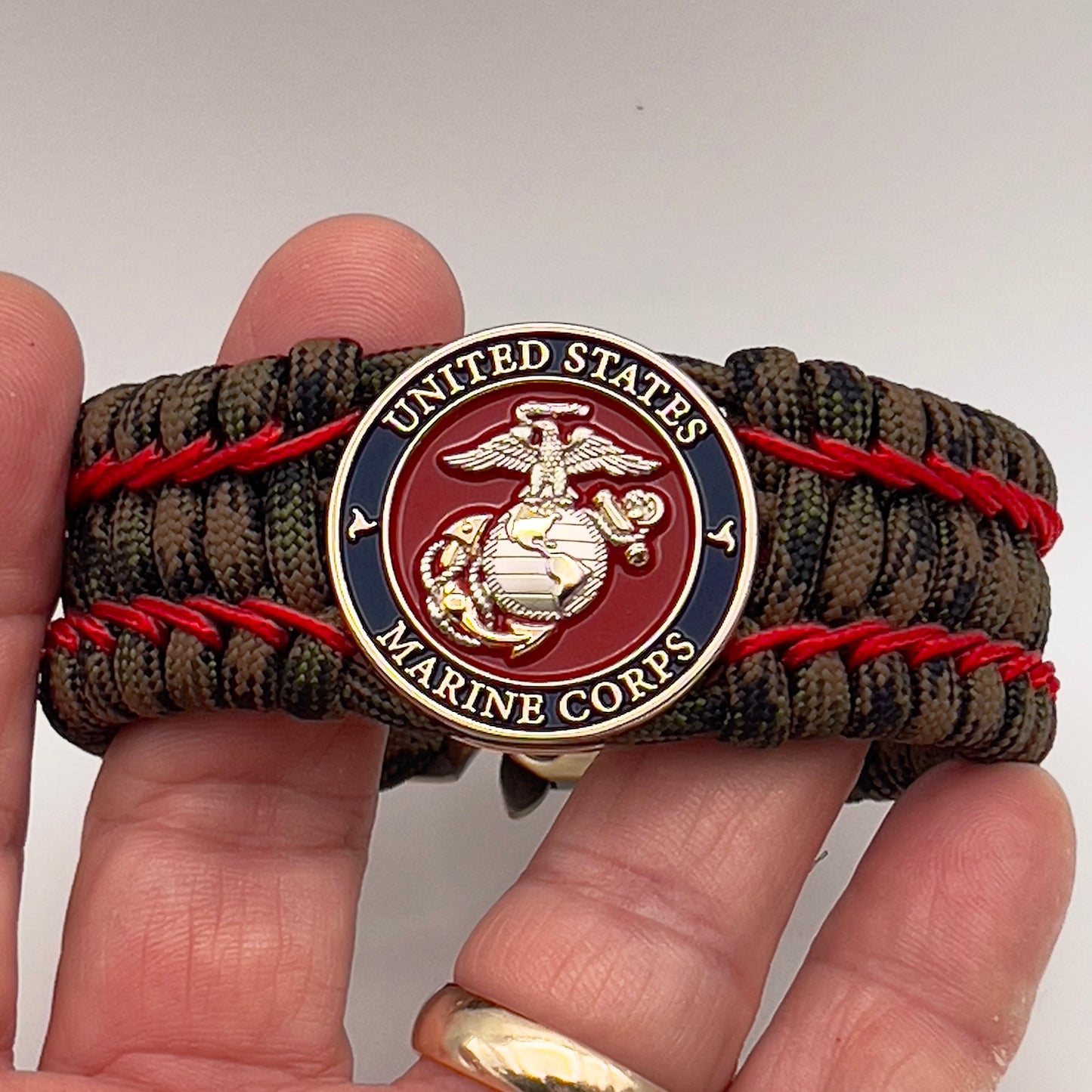 Thick, rigid and comfortable braided United States Marine Corps bracelet featuring a 24K gold and silver plated USMC officer Eagle Globe and Anchor medallion, a gold Cobra style tactical buckle and woven with Woodland Camo 550 paracord and Imperial Red micro cord.
