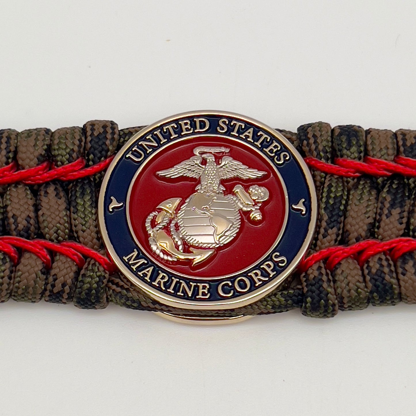Thick, rigid and comfortable braided United States Marine Corps bracelet featuring a 24K gold and silver plated USMC officer Eagle Globe and Anchor medallion, a gold Cobra style tactical buckle and woven with Woodland Camo 550 paracord and Imperial Red micro cord.