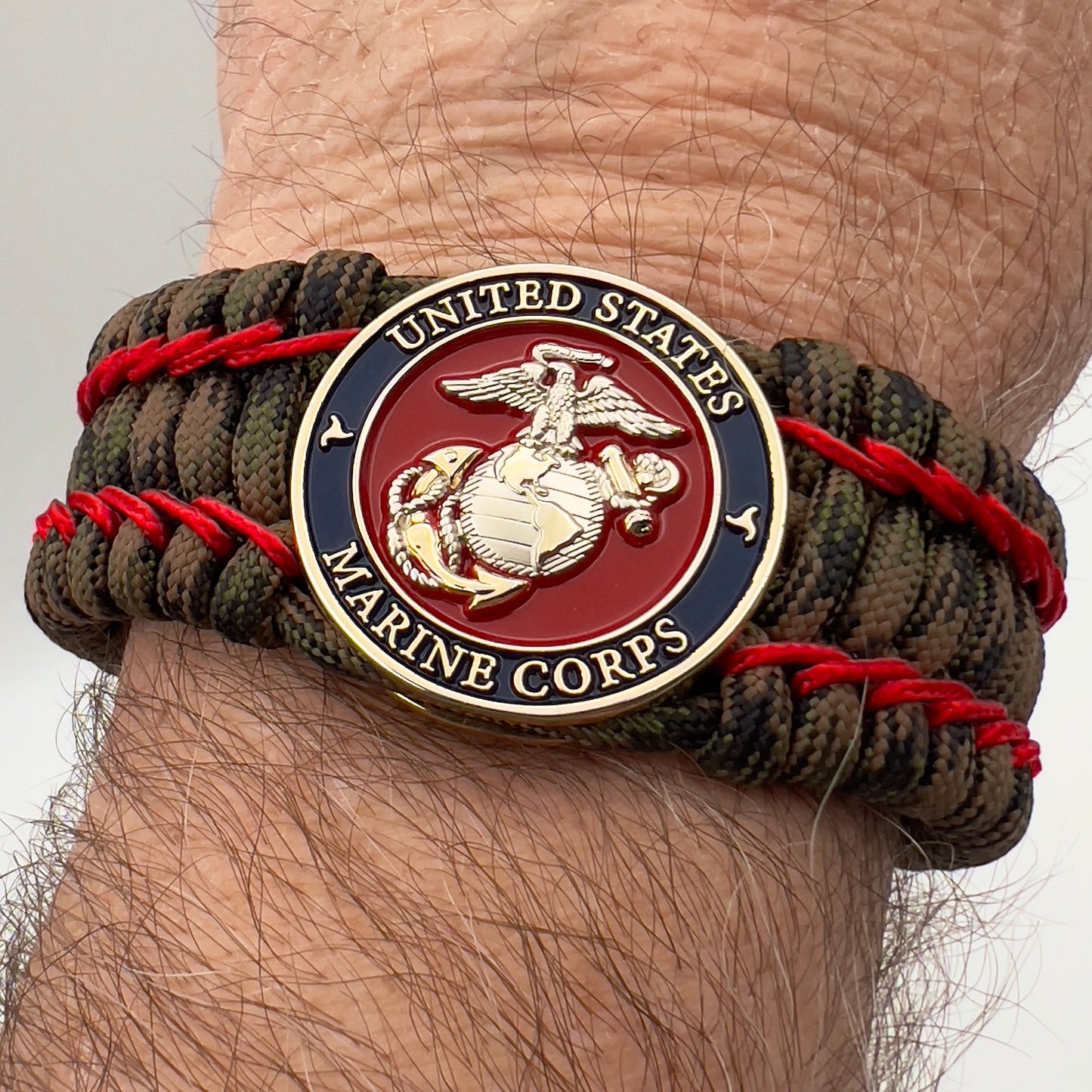 Thick, rigid and comfortable braided United States Marine Corps bracelet featuring a 24K gold and silver plated USMC officer Eagle Globe and Anchor medallion, a gold Cobra style tactical buckle and woven with Woodland Camo 550 paracord and Imperial Red micro cord.