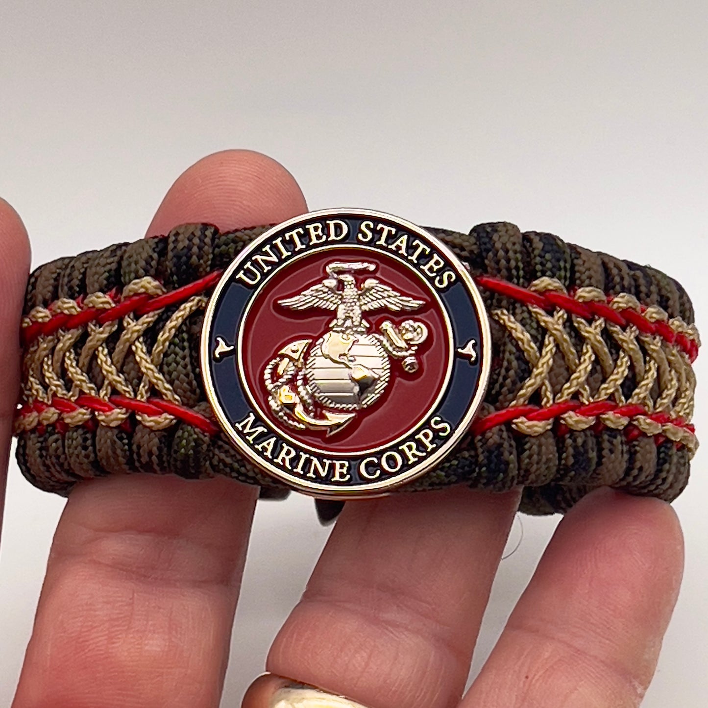 Thick, rigid and comfortable braided United States Marine Corps bracelet featuring a 24K gold and silver plated USMC officer Eagle Globe and Anchor medallion, a gold Cobra style tactical buckle and woven with Woodland Camo 550 paracord and Imperial Red and gold micro cord.