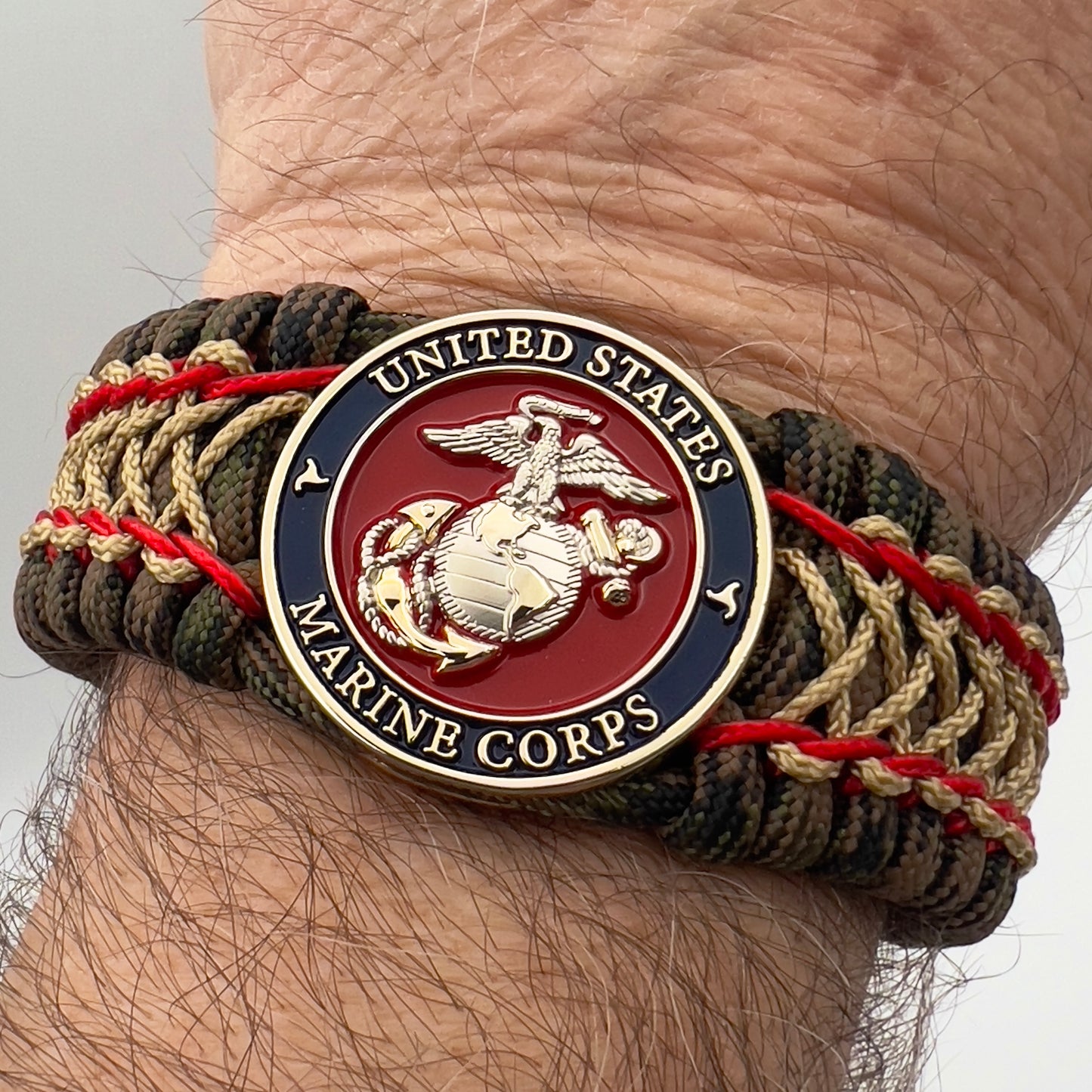 Thick, rigid and comfortable braided United States Marine Corps bracelet featuring a 24K gold and silver plated USMC officer Eagle Globe and Anchor medallion, a gold Cobra style tactical buckle and woven with Woodland Camo 550 paracord and Imperial Red and gold micro cord.