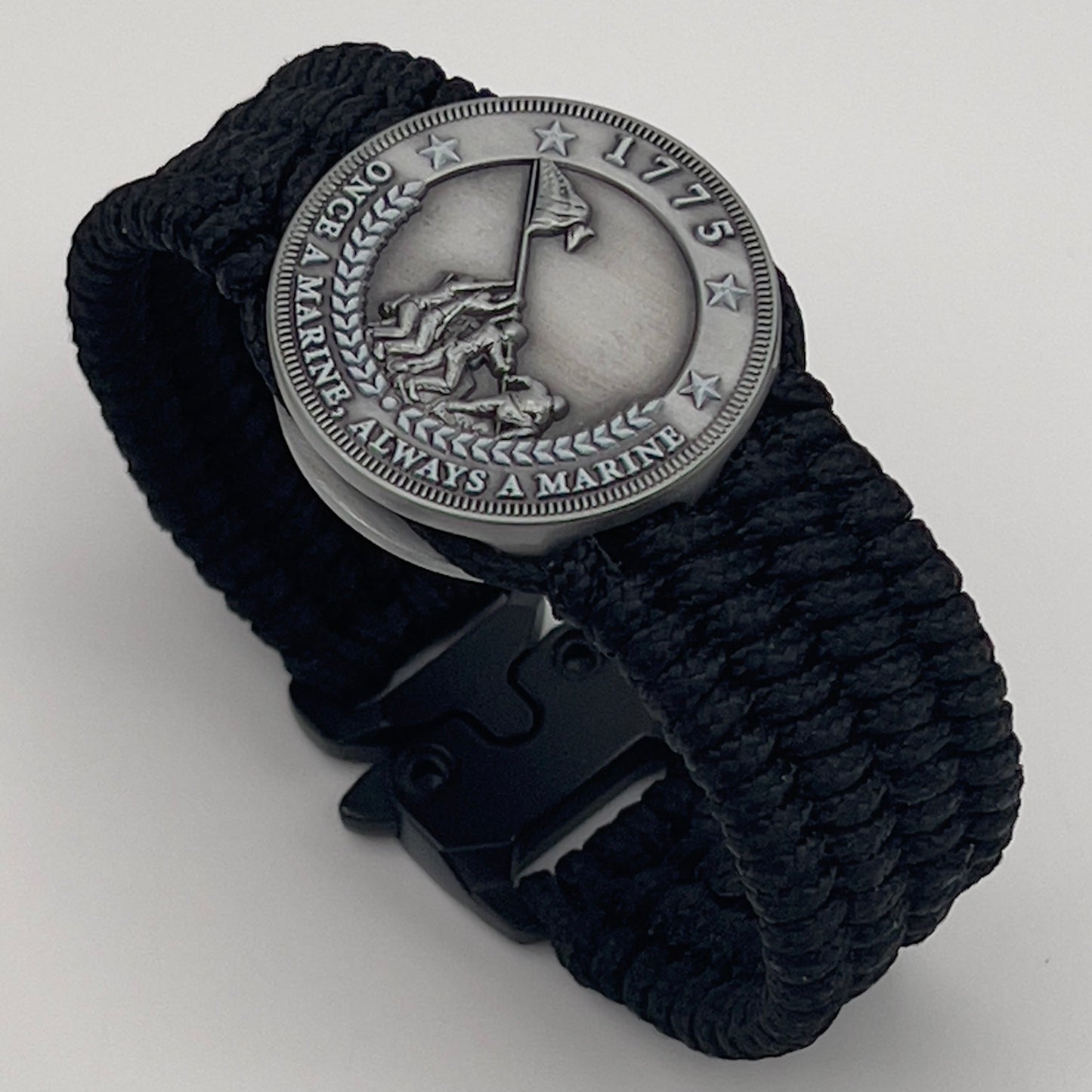 Thin, wide, flexible and comfortable braided United States Marine Corps Iwo Jima bracelet featuring an antique silver plated Iwo Jima flag raising medallion, a black Eagel, Globe and Anchor engraving, a black Cobra style tactical buckle and woven with black Type-1 paracord.