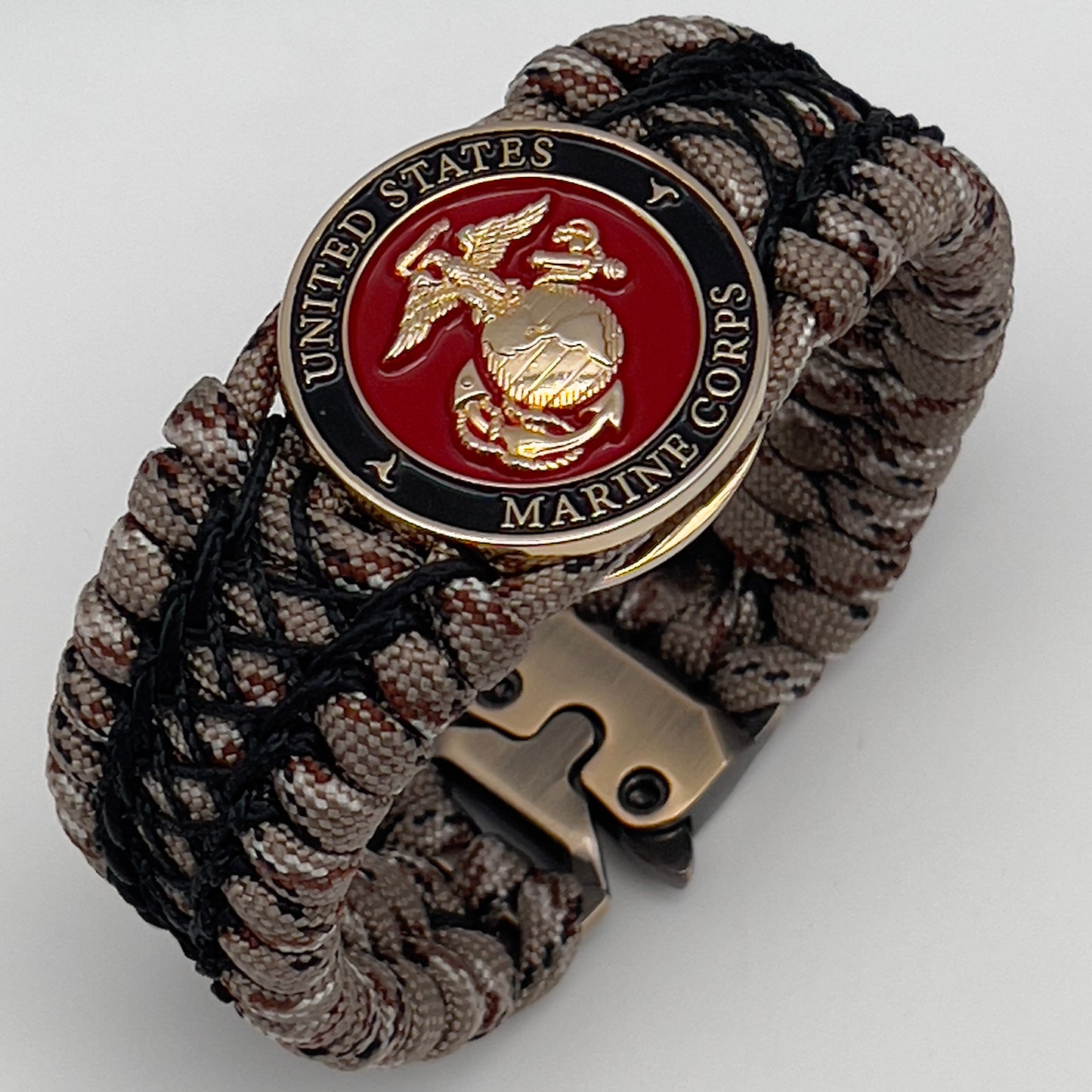 Thick, wide, rigid and comfortable braided United States Marine Corps bracelet featuring a 24K gold plated USMC Eagle Globe and Anchor medallion, a gold Cobra style tactical buckle and woven with Desert Camo 550 paracord and black nano and micro cord.