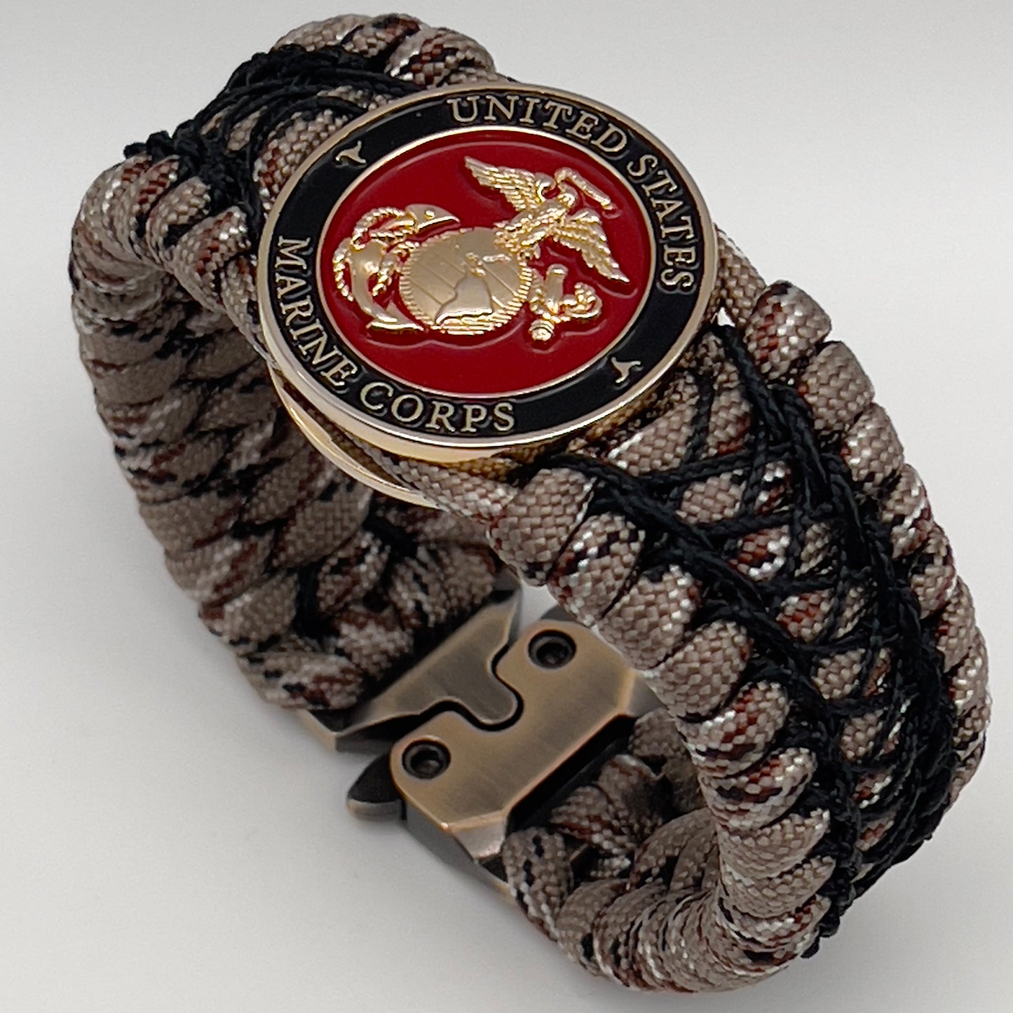 Thick, wide, rigid and comfortable braided United States Marine Corps bracelet featuring a 24K gold plated USMC Eagle Globe and Anchor medallion, a gold Cobra style tactical buckle and woven with Desert Camo 550 paracord and black nano and micro cord.