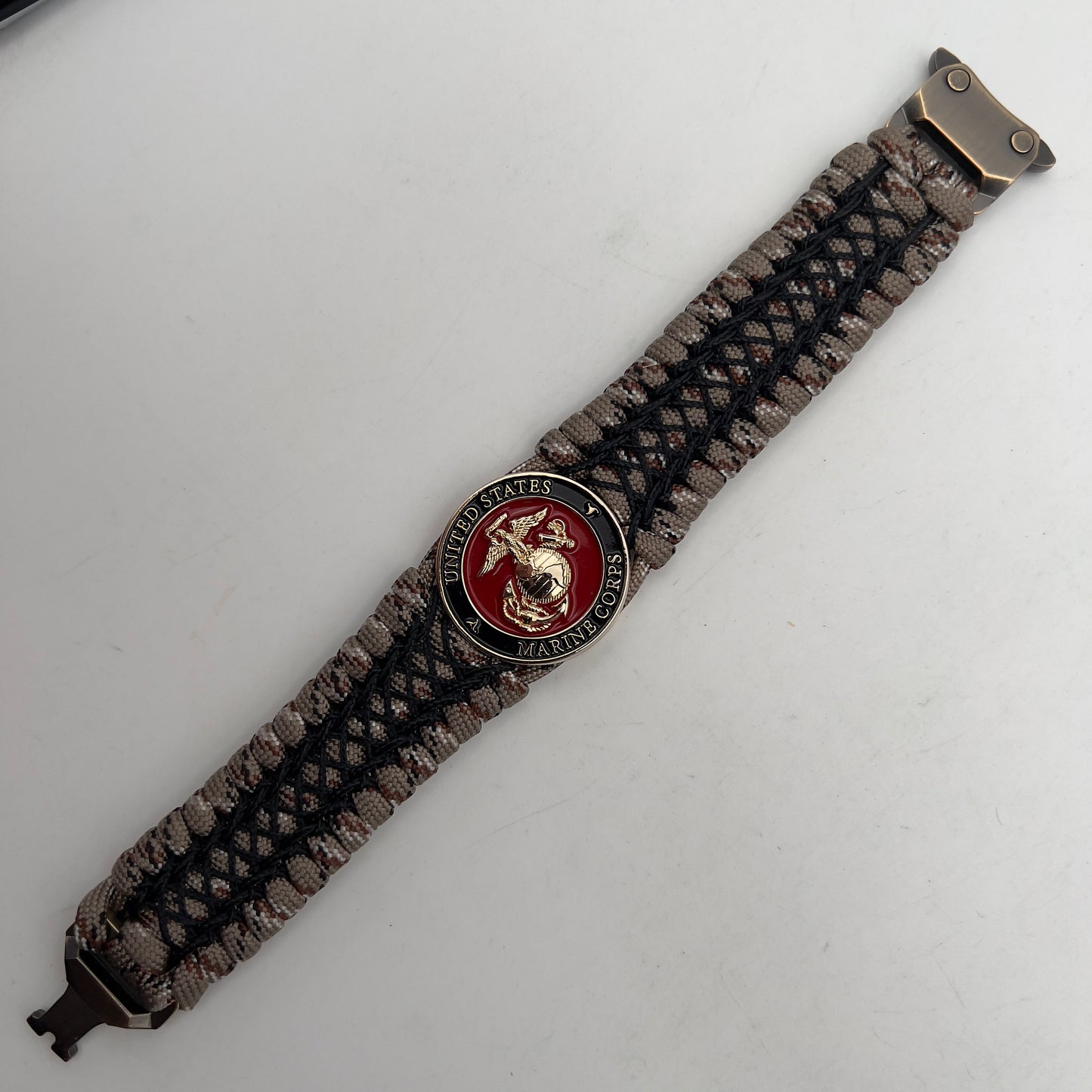 Thick, wide, rigid and comfortable braided United States Marine Corps bracelet featuring a 24K gold plated USMC Eagle Globe and Anchor medallion, a gold Cobra style tactical buckle and woven with Desert Camo 550 paracord and black nano and micro cord.