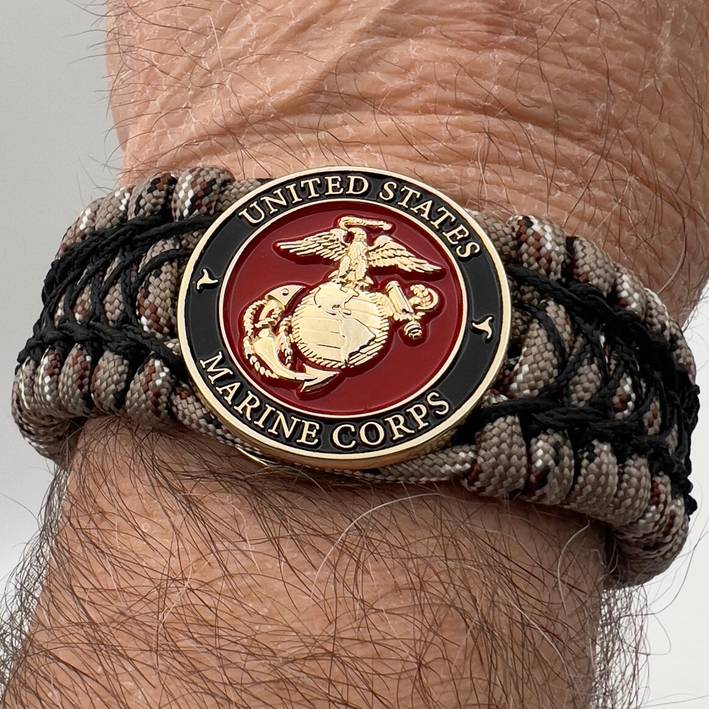 Thick, wide, rigid and comfortable braided United States Marine Corps bracelet featuring a 24K gold plated USMC Eagle Globe and Anchor medallion, a gold Cobra style tactical buckle and woven with Desert Camo 550 paracord and black nano and micro cord.