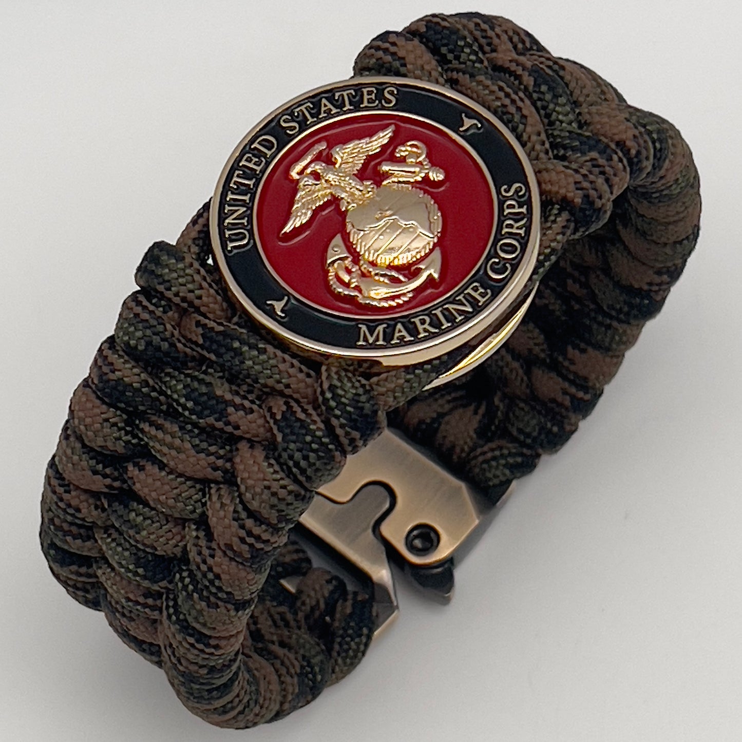 Thick, wide, semi-rigid and comfortable braided United States Marine Corps bracelet featuring a 24K gold plated USMC Eagle Globe and Anchor medallion, a gold Cobra style tactical buckle and woven with Woodland Camo 550 paracord.