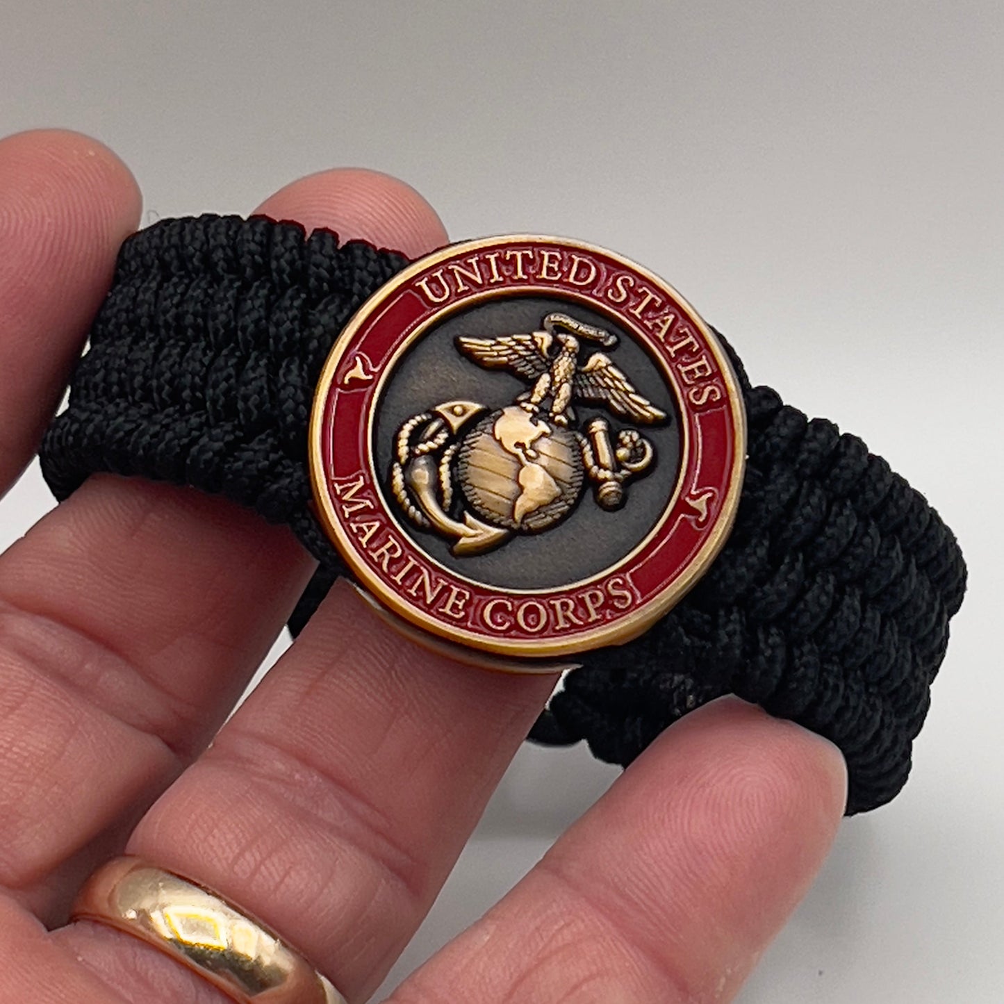 Thin, wide, very flexible and comfortable braided United States Marine Corps bracelet featuring a 24K antique gold plated USMC Eagle Globe and Anchor medallion engraved with the Punisher logo, a black Cobra style tactical buckle and woven with black Type-1 paracord.