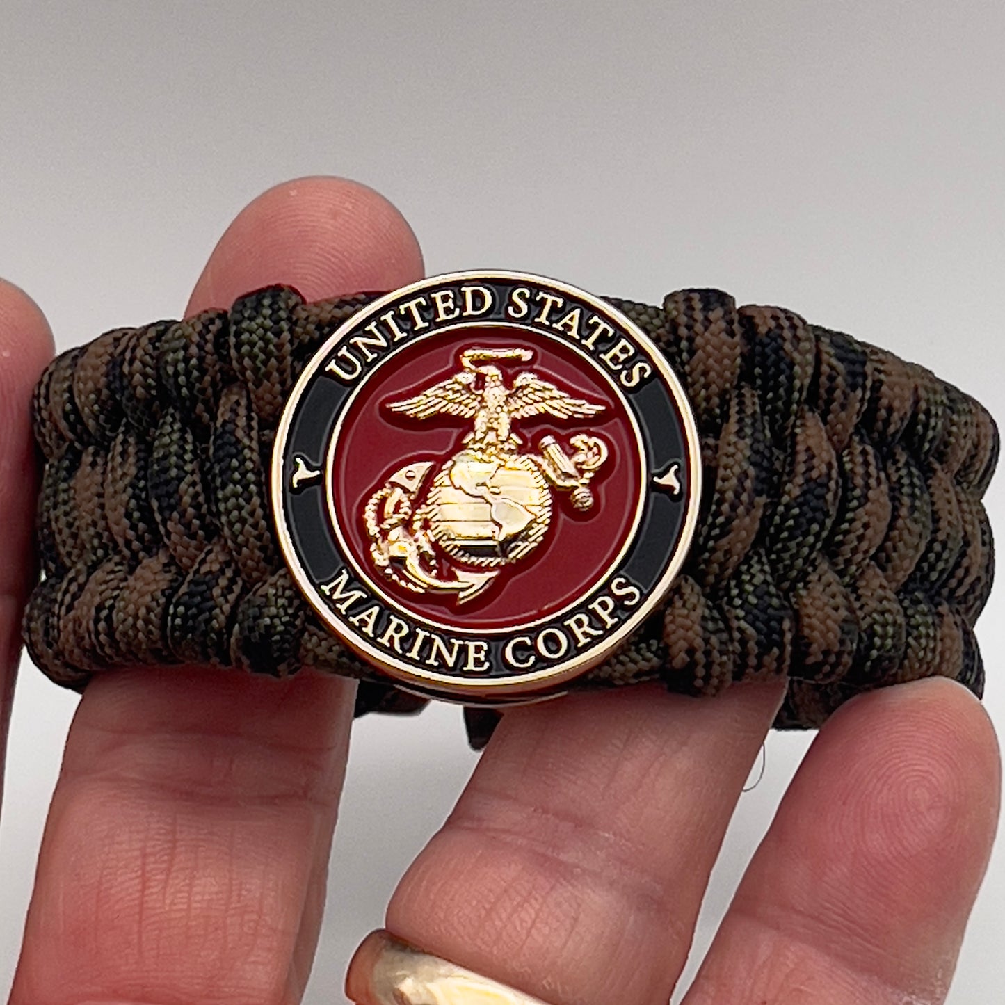 Thick, wide, semi-rigid and comfortable braided United States Marine Corps bracelet featuring a 24K gold plated USMC Eagle Globe and Anchor medallion, a gold Cobra style tactical buckle and woven with Woodland Camo 550 paracord.