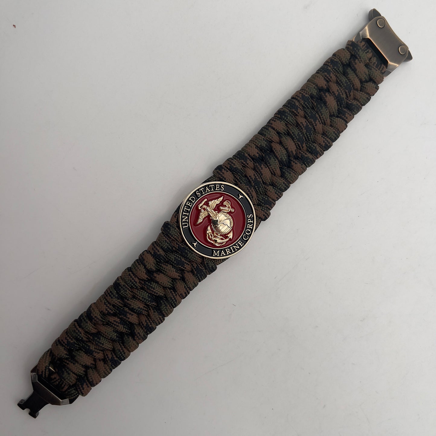 Thick, wide, semi-rigid and comfortable braided United States Marine Corps bracelet featuring a 24K gold plated USMC Eagle Globe and Anchor medallion, a gold Cobra style tactical buckle and woven with Woodland Camo 550 paracord.
