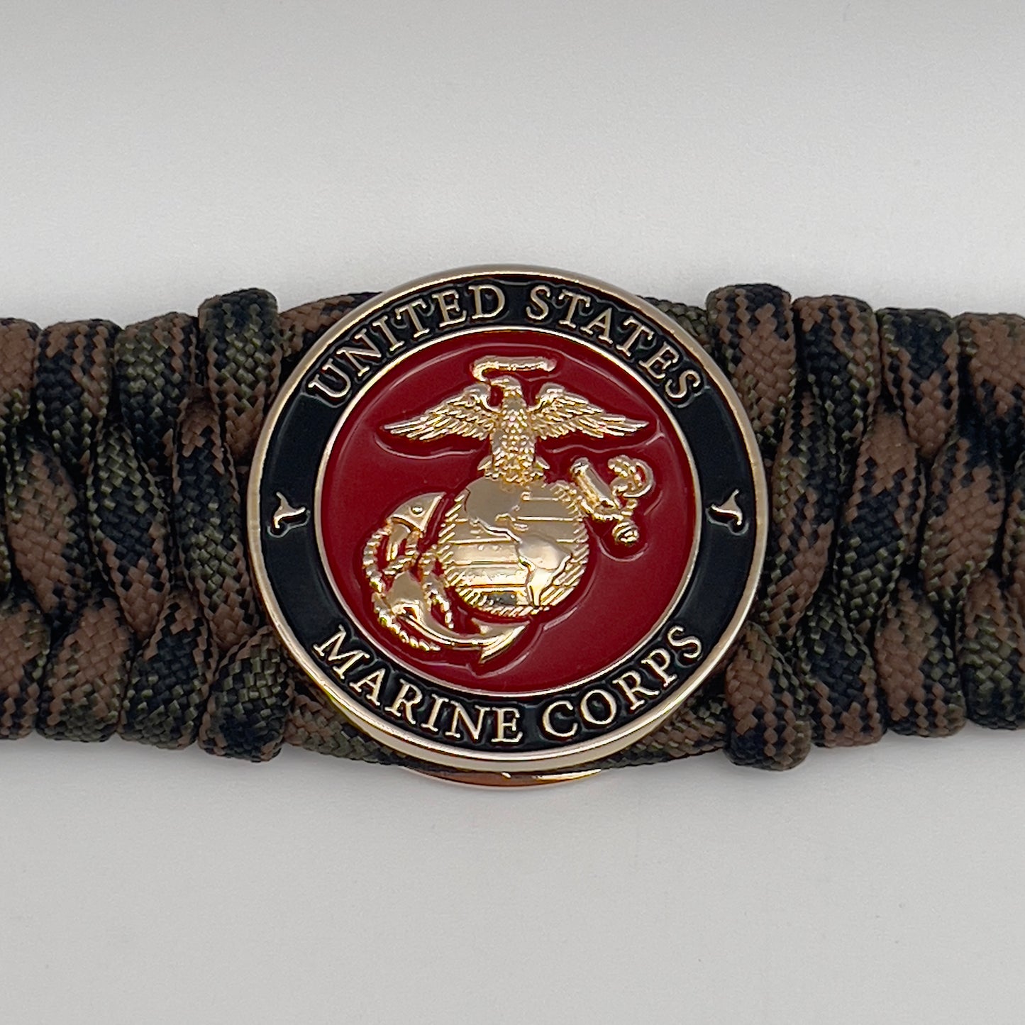 Thick, wide, semi-rigid and comfortable braided United States Marine Corps bracelet featuring a 24K gold plated USMC Eagle Globe and Anchor medallion, a gold Cobra style tactical buckle and woven with Woodland Camo 550 paracord.