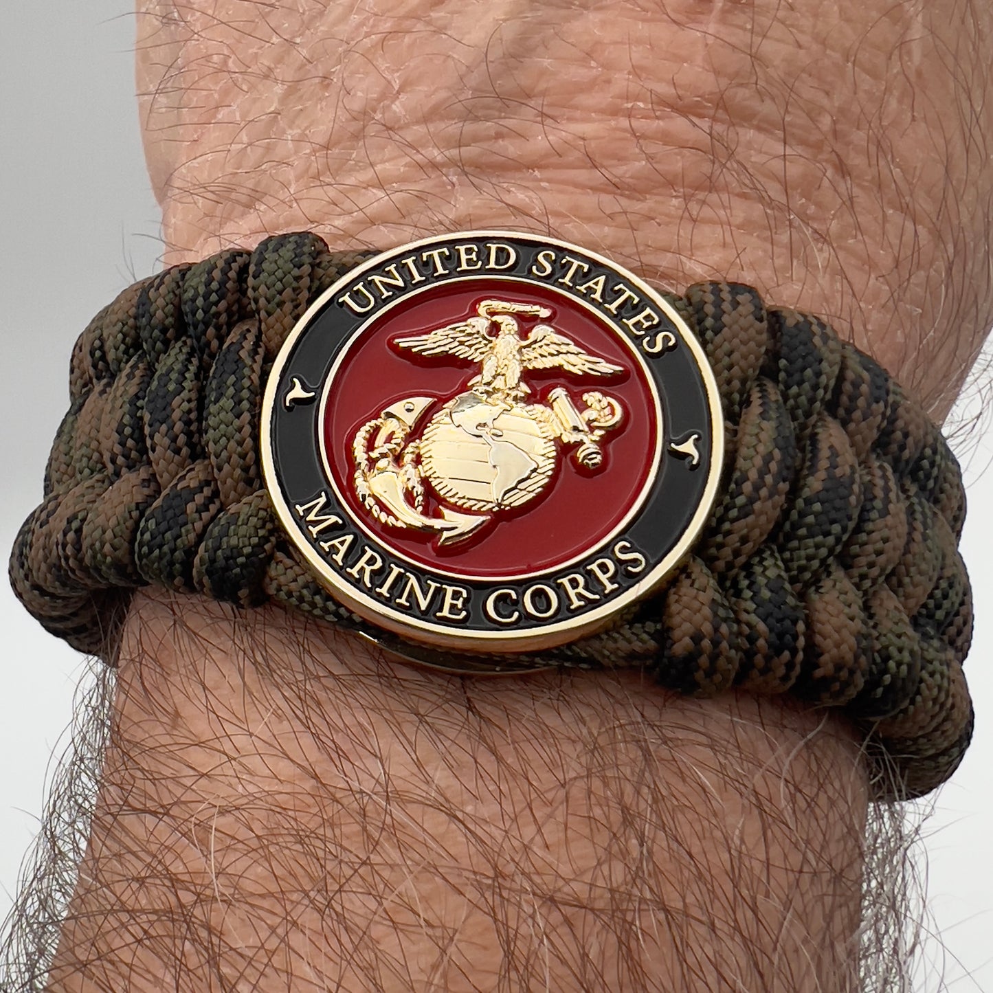 Thick, wide, semi-rigid and comfortable braided United States Marine Corps bracelet featuring a 24K gold plated USMC Eagle Globe and Anchor medallion, a gold Cobra style tactical buckle and woven with Woodland Camo 550 paracord.