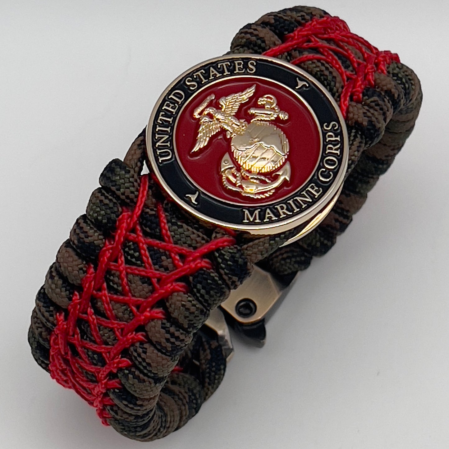 Thick, wide, rigid and comfortable braided United States Marine Corps bracelet featuring a 24K gold plated USMC Eagle Globe and Anchor medallion, a gold Cobra style tactical buckle and woven with Woodland Camo 550 paracord and Imperial Red nano and micro cord.