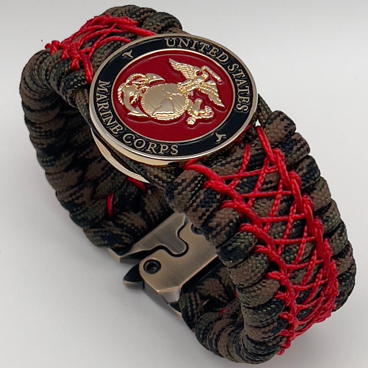 Thick, wide, rigid and comfortable braided United States Marine Corps bracelet featuring a 24K gold plated USMC Eagle Globe and Anchor medallion, a gold Cobra style tactical buckle and woven with Woodland Camo 550 paracord and Imperial Red nano and micro cord.