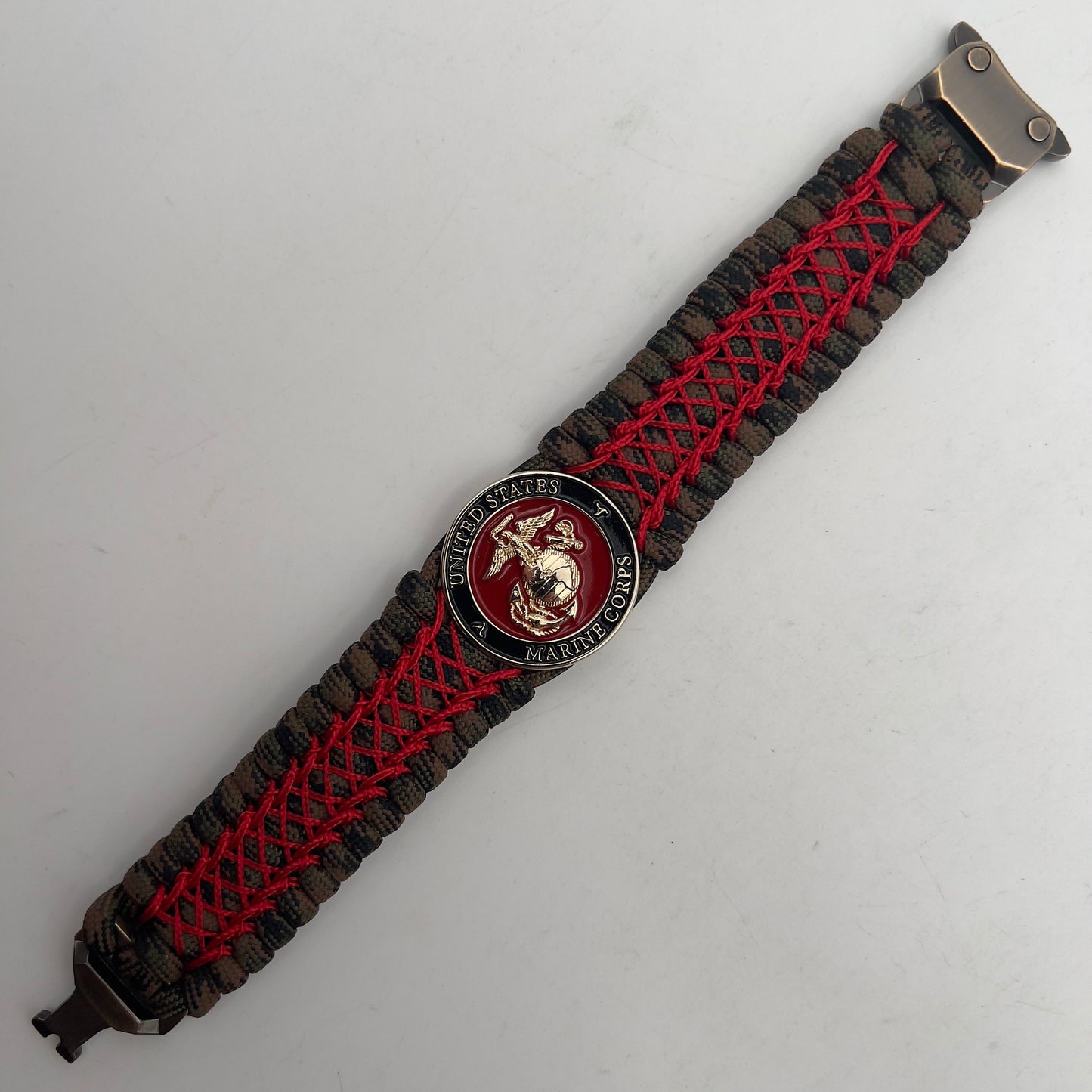 Thick, wide, rigid and comfortable braided United States Marine Corps bracelet featuring a 24K gold plated USMC Eagle Globe and Anchor medallion, a gold Cobra style tactical buckle and woven with Woodland Camo 550 paracord and Imperial Red nano and micro cord.