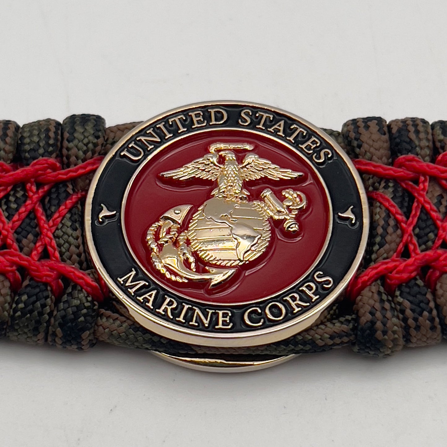 Thick, wide, rigid and comfortable braided United States Marine Corps bracelet featuring a 24K gold plated USMC Eagle Globe and Anchor medallion, a gold Cobra style tactical buckle and woven with Woodland Camo 550 paracord and Imperial Red nano and micro cord.