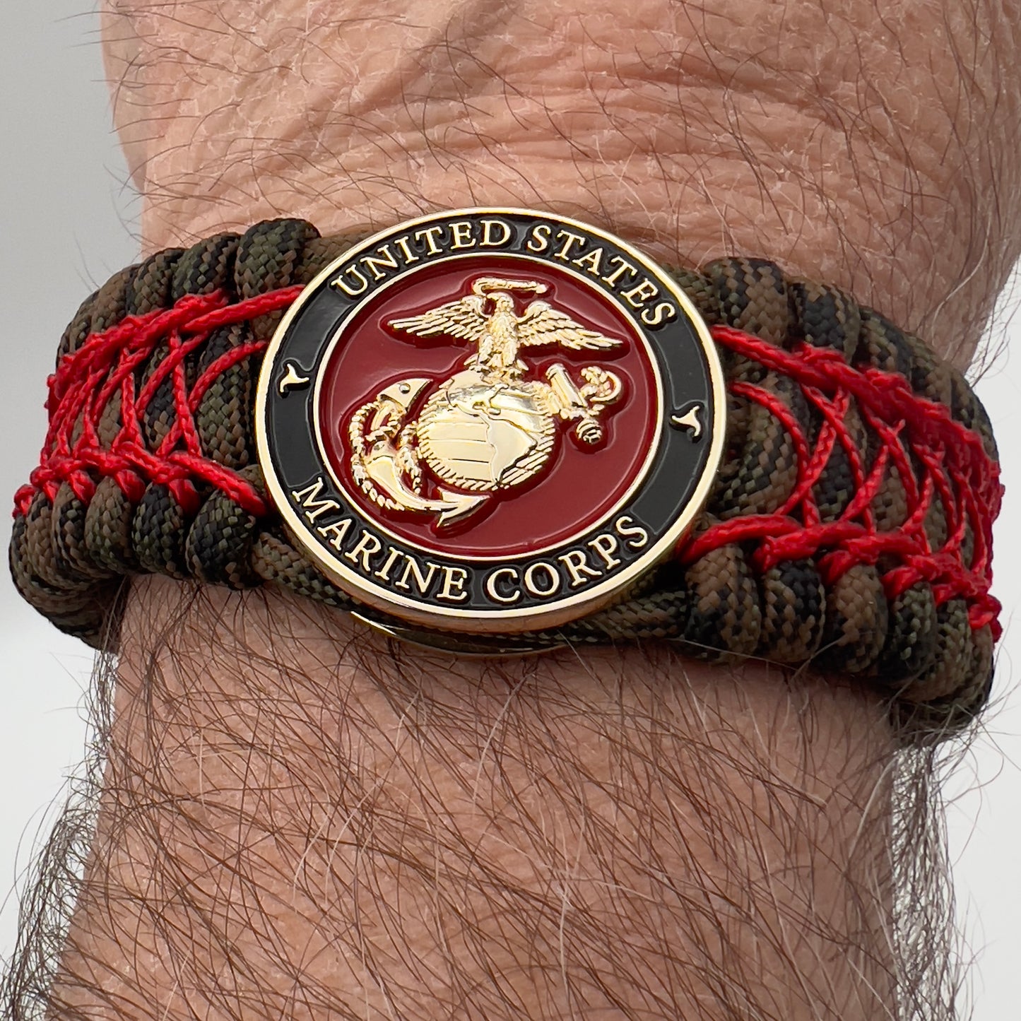 Thick, wide, rigid and comfortable braided United States Marine Corps bracelet featuring a 24K gold plated USMC Eagle Globe and Anchor medallion, a gold Cobra style tactical buckle and woven with Woodland Camo 550 paracord and Imperial Red nano and micro cord.
