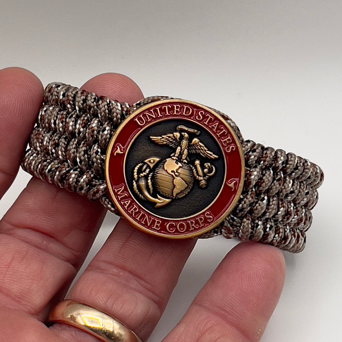 Thin, wide, very flexible and comfortable braided United States Marine Corps bracelet featuring a 24K antique gold plated USMC Eagle Globe and Anchor medallion engraved with the Punisher logo, a gold Cobra style tactical buckle and woven with Desert Camo Type-1 paracord.