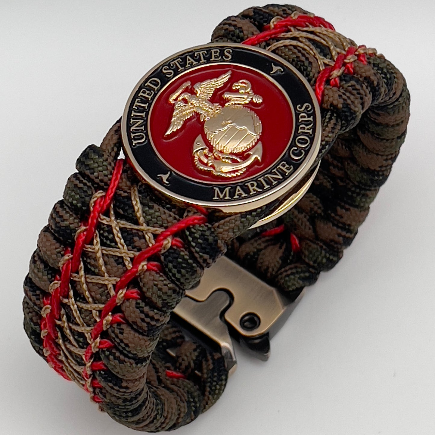 Thick, wide, rigid and comfortable braided United States Marine Corps bracelet featuring a 24K gold plated USMC Eagle Globe and Anchor medallion, a gold Cobra style tactical buckle and woven with Woodland Camo 550 paracord and Imperial Red micro and gold nano cord.