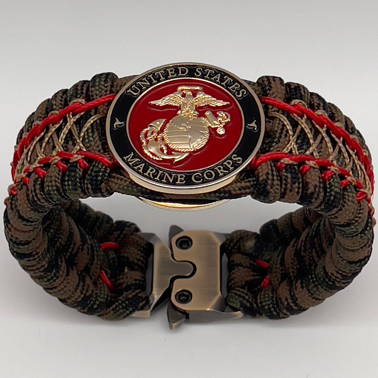 Thick, wide, rigid and comfortable braided United States Marine Corps bracelet featuring a 24K gold plated USMC Eagle Globe and Anchor medallion, a gold Cobra style tactical buckle and woven with Woodland Camo 550 paracord and Imperial Red micro and gold nano cord.