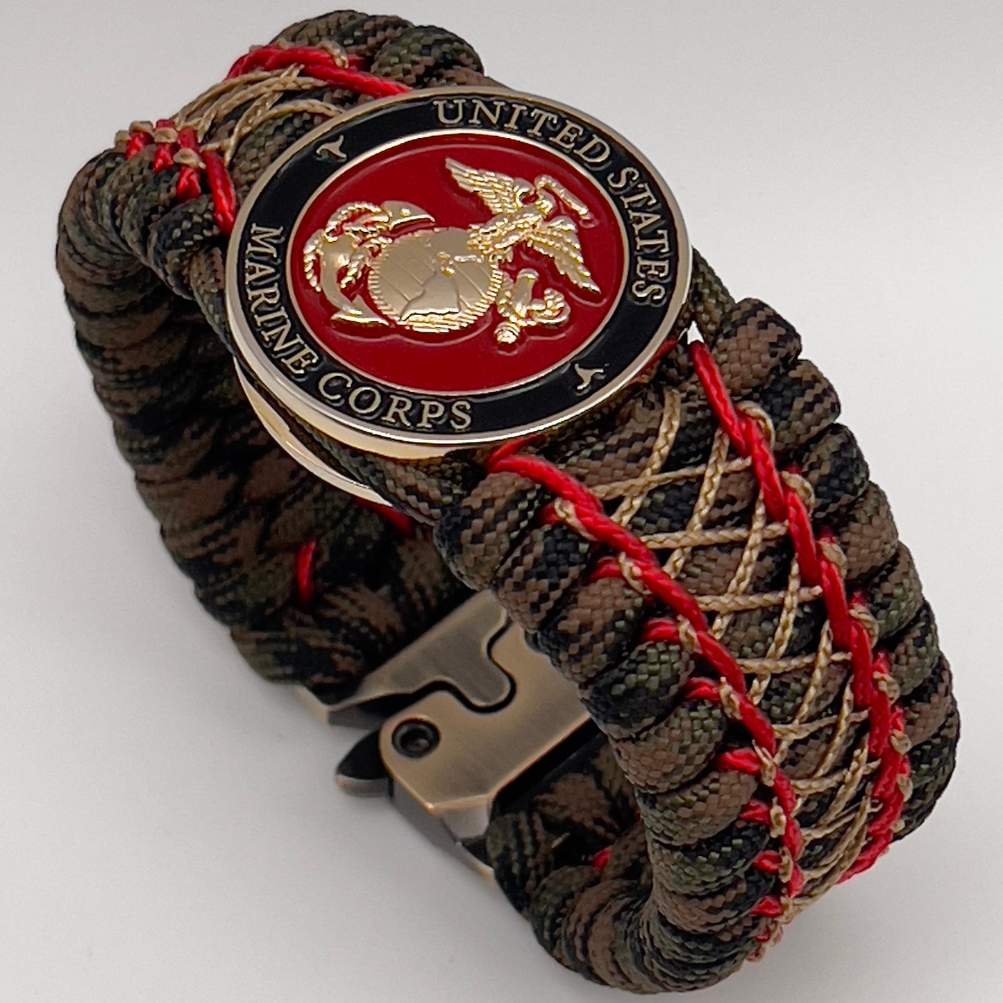 Thick, wide, rigid and comfortable braided United States Marine Corps bracelet featuring a 24K gold plated USMC Eagle Globe and Anchor medallion, a gold Cobra style tactical buckle and woven with Woodland Camo 550 paracord and Imperial Red micro and gold nano cord.