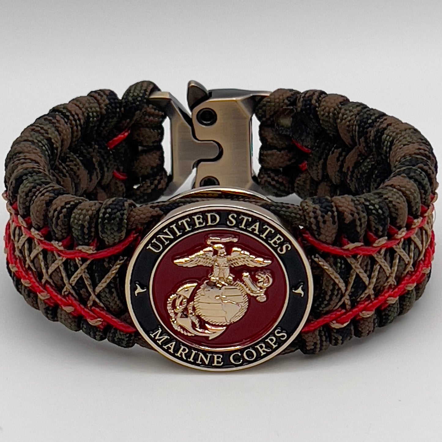 Thick, wide, rigid and comfortable braided United States Marine Corps bracelet featuring a 24K gold plated USMC Eagle Globe and Anchor medallion, a gold Cobra style tactical buckle and woven with Woodland Camo 550 paracord and Imperial Red micro and gold nano cord.