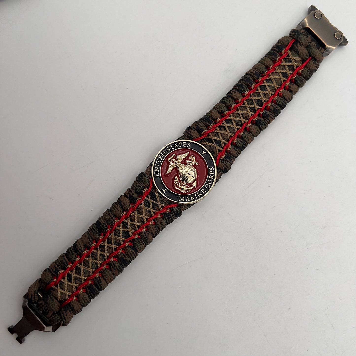 Thick, wide, rigid and comfortable braided United States Marine Corps bracelet featuring a 24K gold plated USMC Eagle Globe and Anchor medallion, a gold Cobra style tactical buckle and woven with Woodland Camo 550 paracord and Imperial Red micro and gold nano cord.