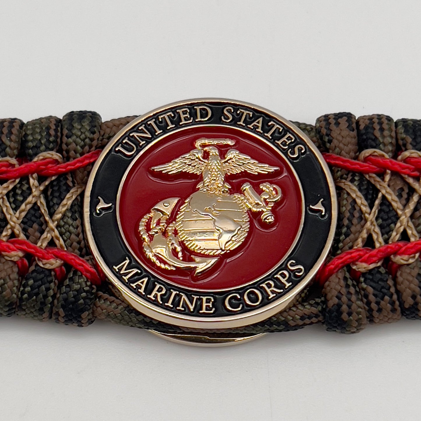 Thick, wide, rigid and comfortable braided United States Marine Corps bracelet featuring a 24K gold plated USMC Eagle Globe and Anchor medallion, a gold Cobra style tactical buckle and woven with Woodland Camo 550 paracord and Imperial Red micro and gold nano cord.