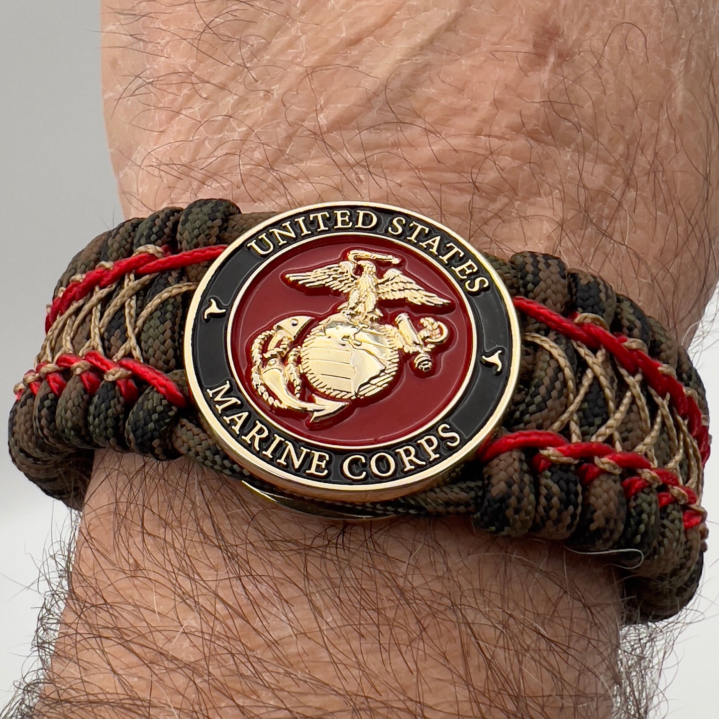 Thick, wide, rigid and comfortable braided United States Marine Corps bracelet featuring a 24K gold plated USMC Eagle Globe and Anchor medallion, a gold Cobra style tactical buckle and woven with Woodland Camo 550 paracord and Imperial Red micro and gold nano cord.