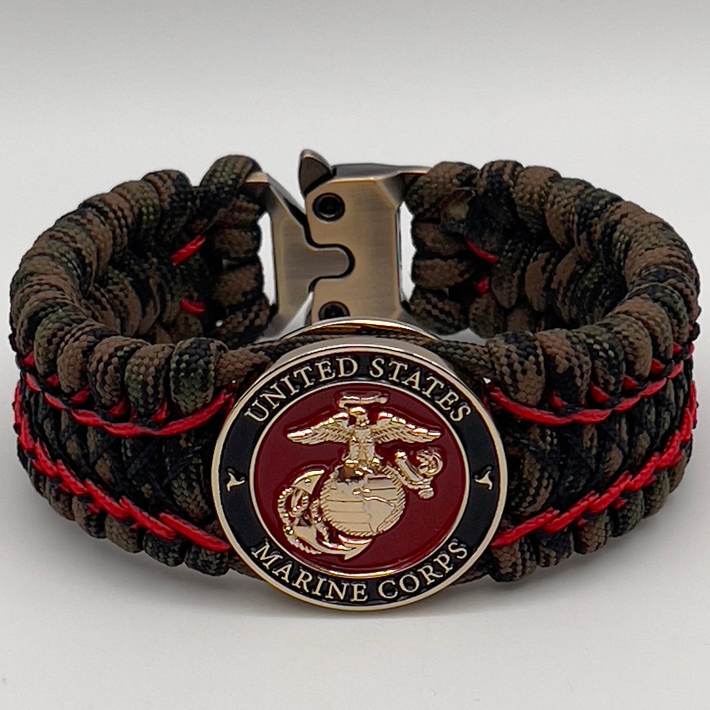 Thick, wide, rigid and comfortable braided United States Marine Corps bracelet featuring a 24K gold plated USMC Eagle Globe and Anchor medallion, a gold Cobra style tactical buckle and woven with Woodland Camo 550 paracord and Imperial Red micro and black nano cord.