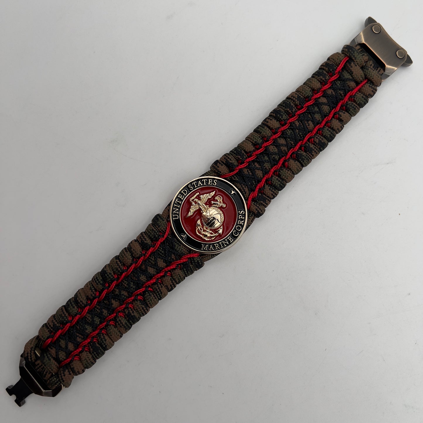 Thick, wide, rigid and comfortable braided United States Marine Corps bracelet featuring a 24K gold plated USMC Eagle Globe and Anchor medallion, a gold Cobra style tactical buckle and woven with Woodland Camo 550 paracord and Imperial Red micro and black nano cord.
