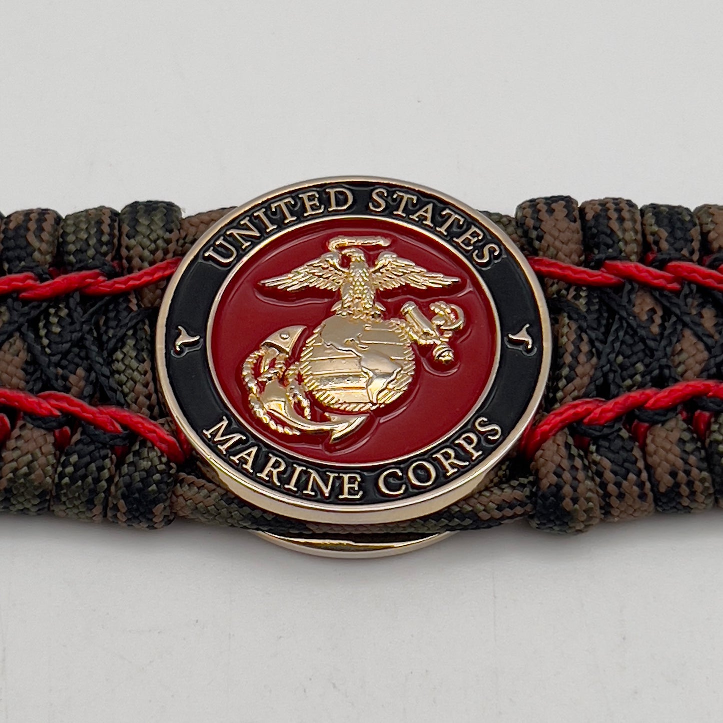Thick, wide, rigid and comfortable braided United States Marine Corps bracelet featuring a 24K gold plated USMC Eagle Globe and Anchor medallion, a gold Cobra style tactical buckle and woven with Woodland Camo 550 paracord and Imperial Red micro and black nano cord.