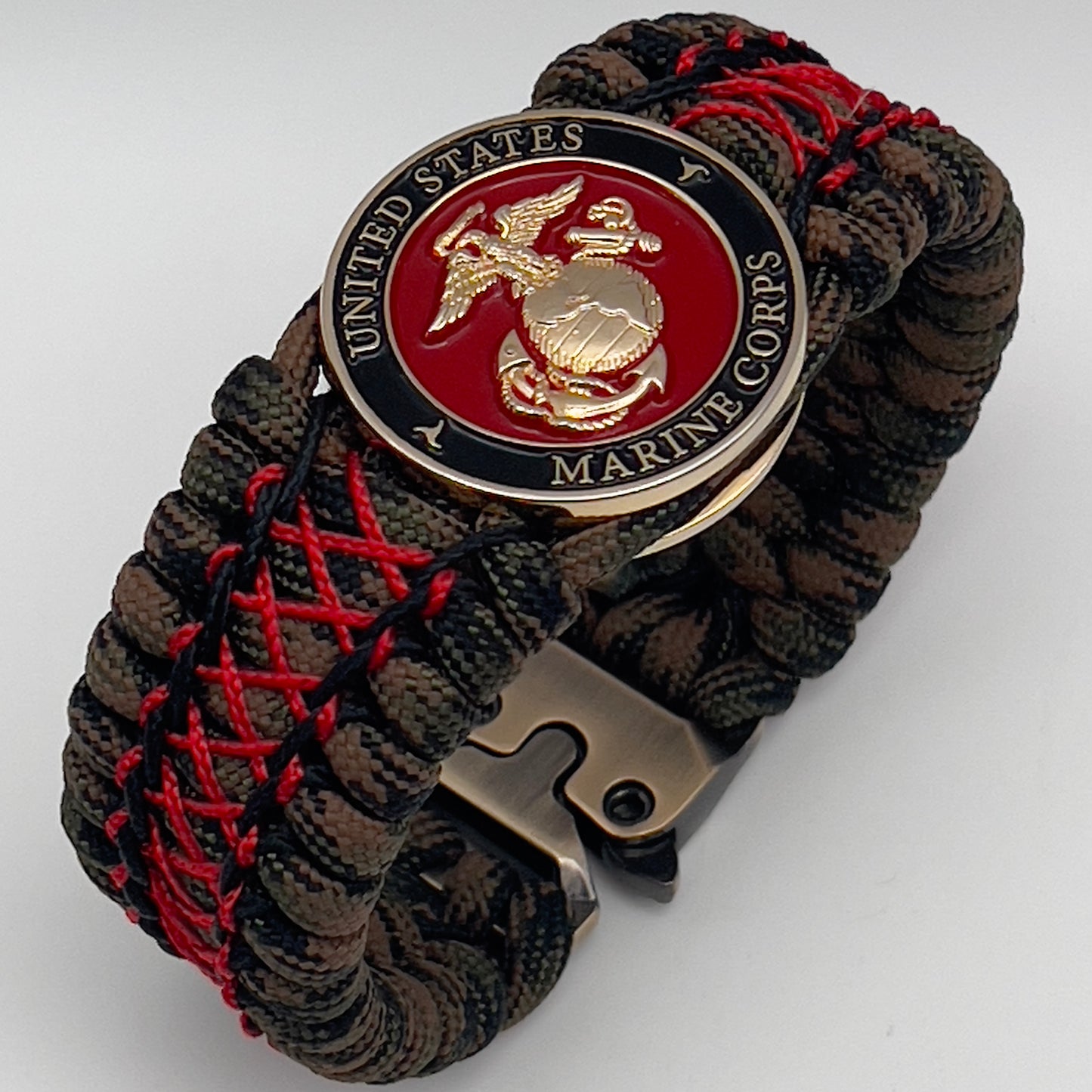 Thick, wide, rigid and comfortable braided United States Marine Corps bracelet featuring a 24K gold plated USMC Eagle Globe and Anchor medallion, a gold Cobra style tactical buckle and woven with Woodland Camo 550 paracord and Imperial Red micro and black nano cord.