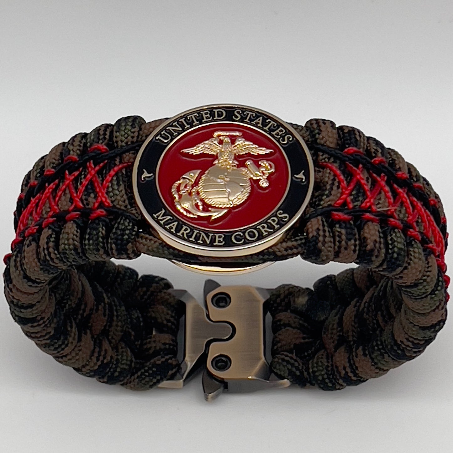 Thick, wide, rigid and comfortable braided United States Marine Corps bracelet featuring a 24K gold plated USMC Eagle Globe and Anchor medallion, a gold Cobra style tactical buckle and woven with Woodland Camo 550 paracord and Imperial Red micro and black nano cord.
