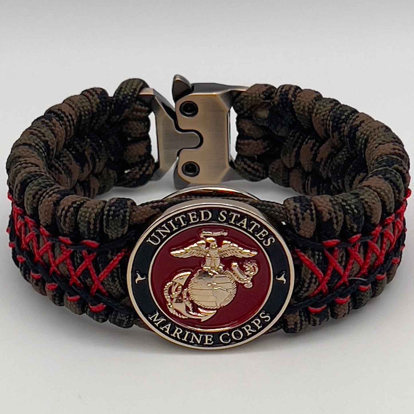 Thick, wide, rigid and comfortable braided United States Marine Corps bracelet featuring a 24K gold plated USMC Eagle Globe and Anchor medallion, a gold Cobra style tactical buckle and woven with Woodland Camo 550 paracord and Imperial Red micro and black nano cord.