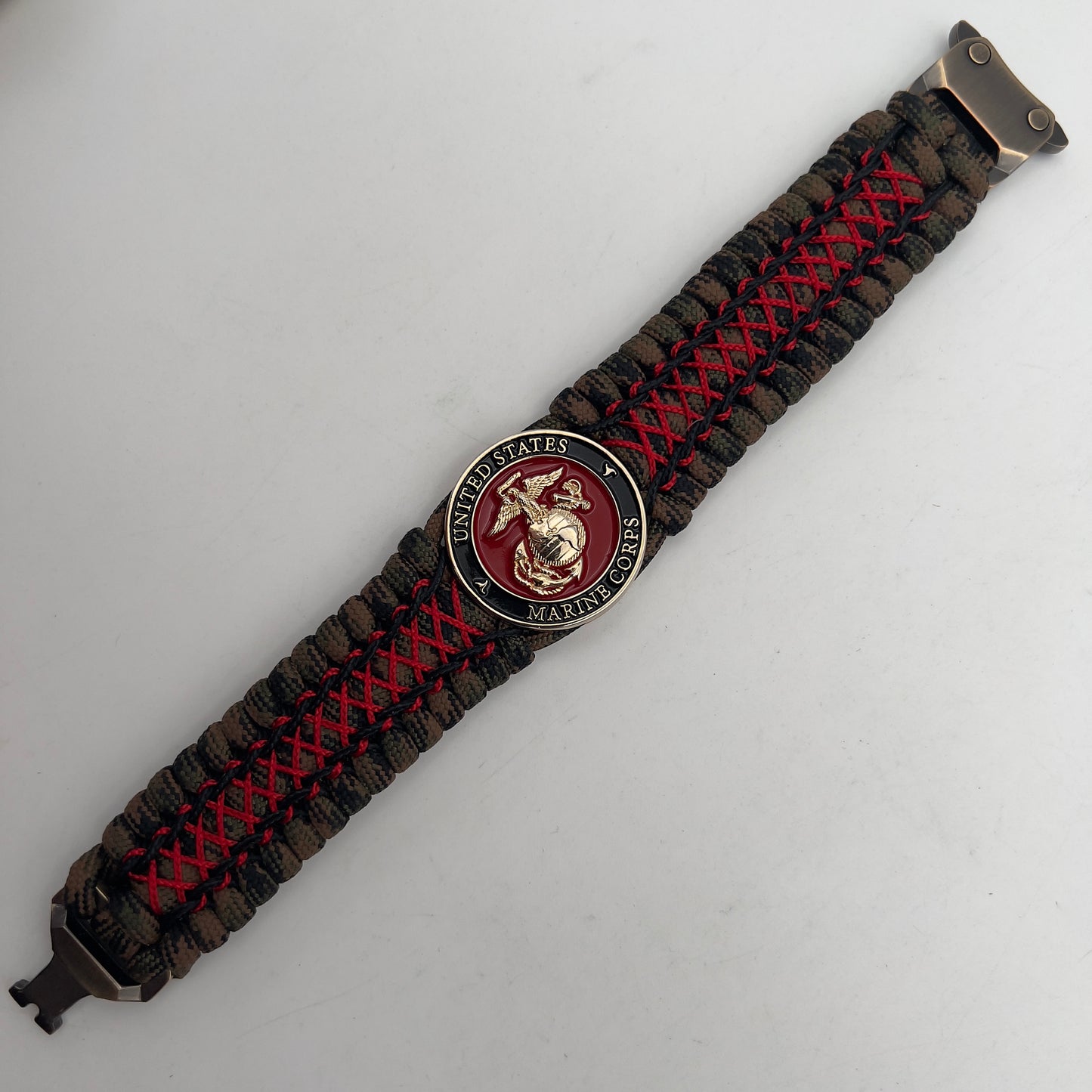 Thick, wide, rigid and comfortable braided United States Marine Corps bracelet featuring a 24K gold plated USMC Eagle Globe and Anchor medallion, a gold Cobra style tactical buckle and woven with Woodland Camo 550 paracord and Imperial Red micro and black nano cord.