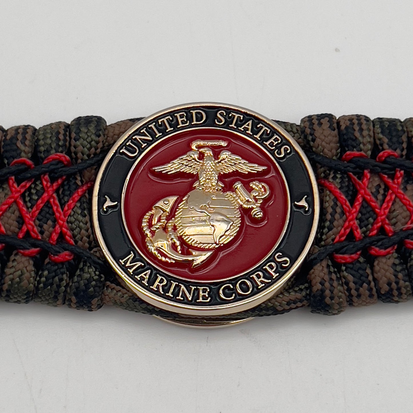 Thick, wide, rigid and comfortable braided United States Marine Corps bracelet featuring a 24K gold plated USMC Eagle Globe and Anchor medallion, a gold Cobra style tactical buckle and woven with Woodland Camo 550 paracord and Imperial Red micro and black nano cord.