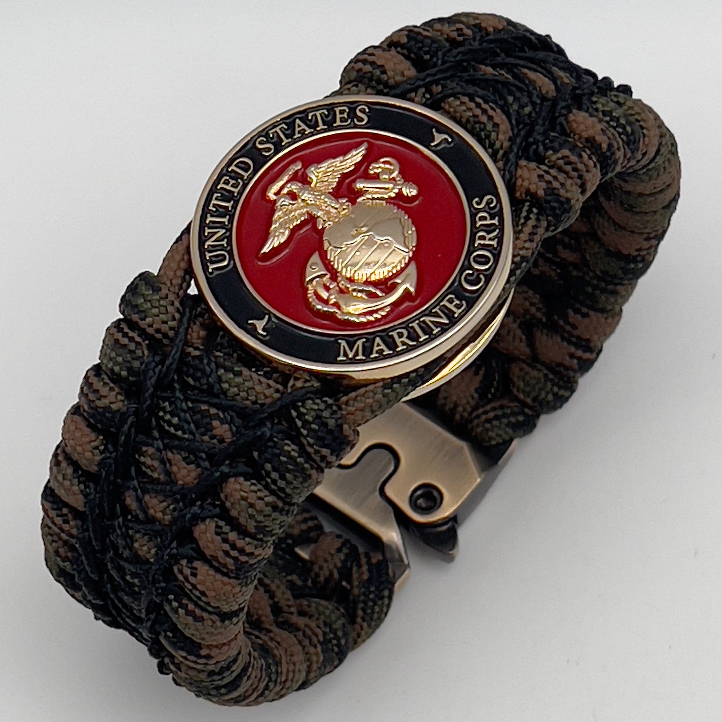 Thick, wide, rigid and comfortable braided United States Marine Corps bracelet featuring a 24K gold plated USMC Eagle Globe and Anchor medallion, a gold Cobra style tactical buckle and woven with Woodland Camo 550 paracord and black nano and micro cord.