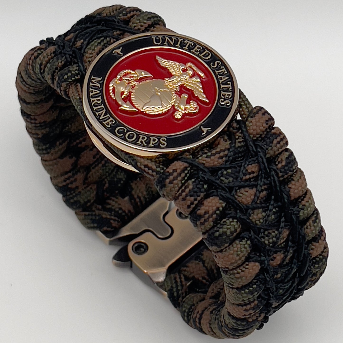 Thick, wide, rigid and comfortable braided United States Marine Corps bracelet featuring a 24K gold plated USMC Eagle Globe and Anchor medallion, a gold Cobra style tactical buckle and woven with Woodland Camo 550 paracord and black nano and micro cord.